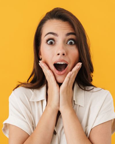 Mujer con expresión de sorpresa, manos en el rostro, sobre fondo amarillo.