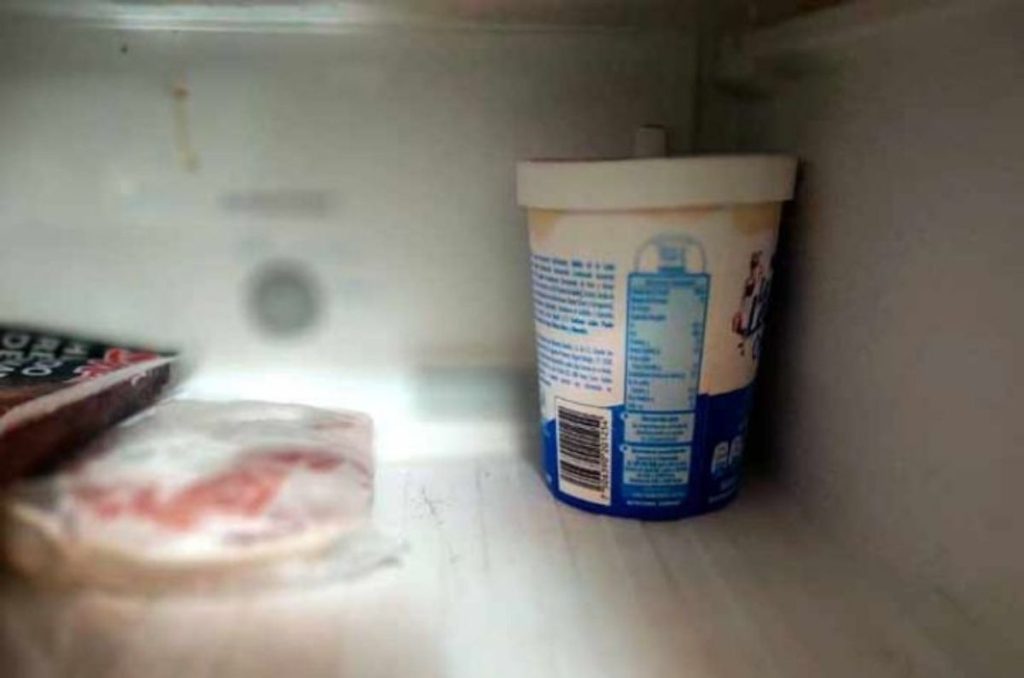 Envase de yogur blanco y azul dentro del refrigerador, usado como recipiente para comida.