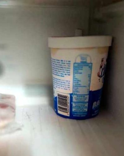 Envase de yogur blanco y azul dentro del refrigerador, usado como recipiente para comida.