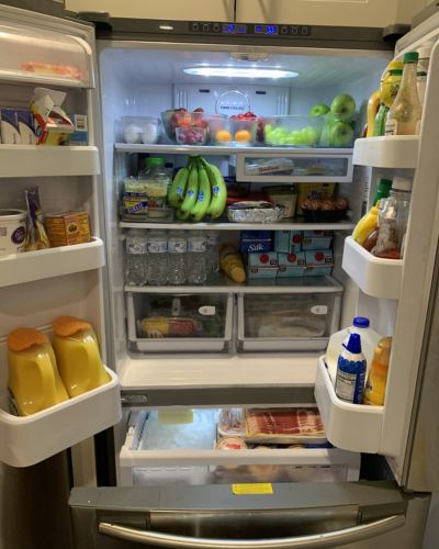 Refrigerador abierto con frutas, verduras y distintos alimentos acomodados en repisas y cajones.