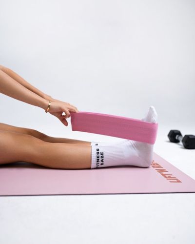 Foto en primer plano de pies sobre un mat color rosa estirando equipo básico para pilates: una banda elastica rosa