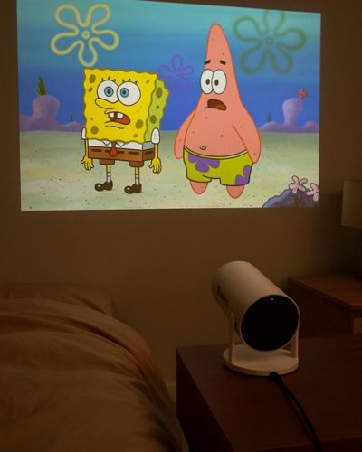 Proyector encendido proyectando caricaturas en una pared, junto a una cama y una mesita de noche.