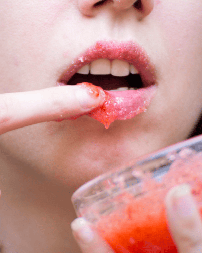 Labios con exfoliante rojo aplicado con el dedo, preparación para unos besos suaves en 14 de Febrero.