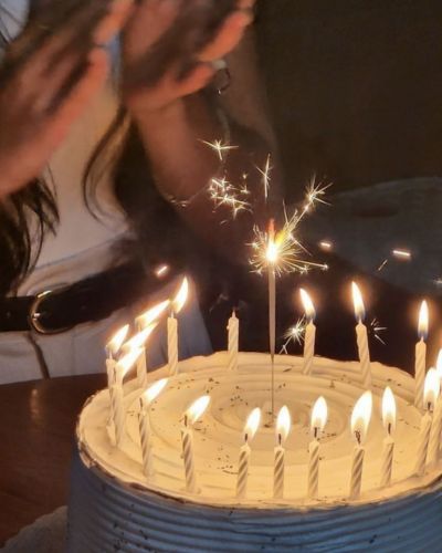 Mantras de cumpleaños: Foto en primer plano de pastel de cumpleaños con velas y mujer de fondo aplaudiendo
