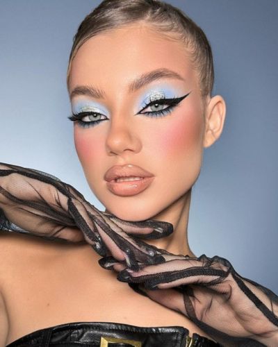 Mujer de tez clara con un maquillaje de ojos celeste, delineado dramático, labios nude y rubor rosado