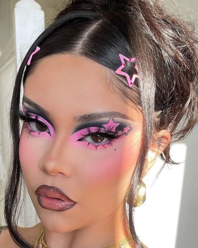 Maquillaje maximaalista en tonos negros y rosa vibrante, con estrellas como decoración en el exterior del ojo