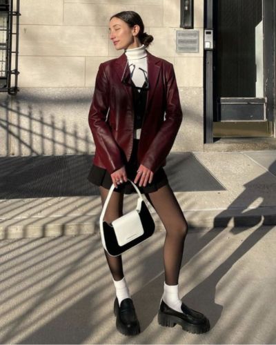 Look con abrigo de cuero en color vino, mini vestido negro, medias negras y blusa de cuello alto blanca