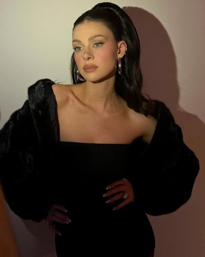 Foto de Nicola Peltz usando un vestido de gala en color negro, con un peinado semi recogido, accesorios minimalistas y maquillaje natural