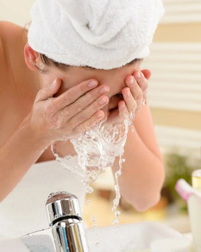 Persona lavándose la cara en el lavabo con agua, paso básico de skincare.