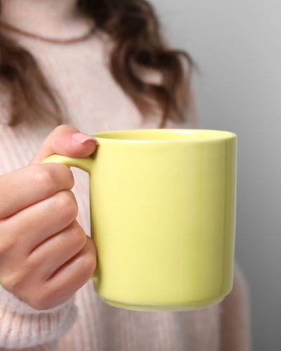 Mano sosteniendo una taza amarilla, momento de pausa y relajación en casa.