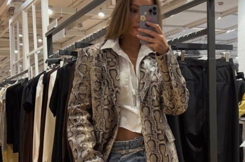 Selfie mujer en el espejo con un outfit casual: pantalón de mezclilla, camisa blanca y gabardina animal print de serpiente