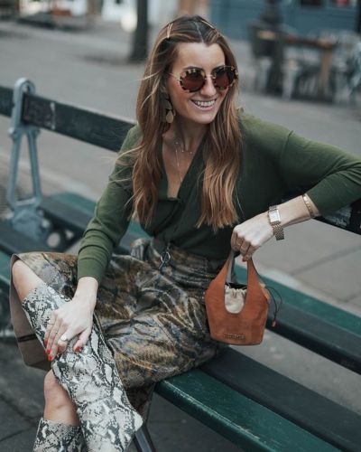Foto de mujer sentada usando botas snake print, blusa verde y falda de cuero animal print 
