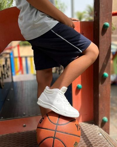 Tips para mantener los tenis blancos de tus hijos limpios. Foto en plano medio de niño usando tenis blancos, shot y camiseta, jugando con un balón de basquet