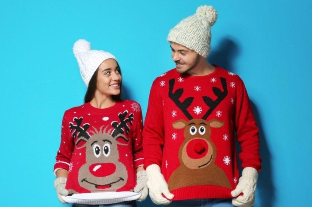 Pareja usando ugly sweaters de reno y renita, sonriendo y disfrutando juntos