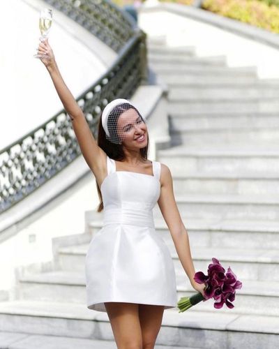Foto de novia al pie de unas escaleras con vestido en corte A y ramo de rosas en la mano