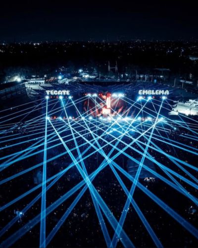 Vista aérea del escenario principal del Tecate Emblema con luces láser azules iluminando el Autódromo Hermanos Rodríguez en la CDMX.