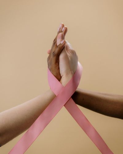 Dos mujeres entrelazan sus manos con un lazo rosa alrededor, símbolo de apoyo y concientización sobre el cáncer de mama.