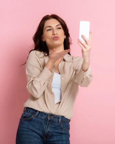 Mujer tomándose una selfie sobre fondo rosa, representando amor propio, autoestima y bienestar emocional en San Valentín.