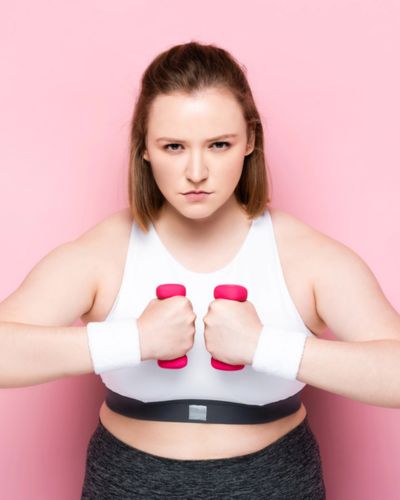 Mujer fuerte sosteniendo mancuernas rosas sobre fondo rosa, representando amor propio, bienestar físico e independencia femenina en San Valentín.