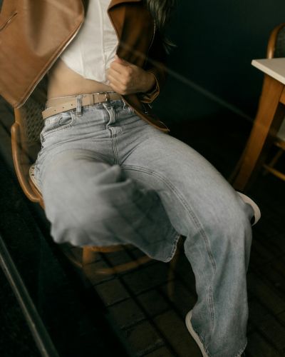 Outfit con jeans rectos, cinturón beige y chamarra de piel café, estilo casual urbano en tendencia.