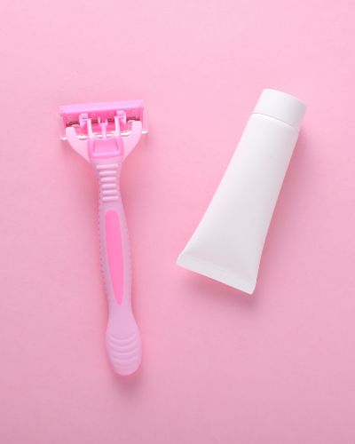 Rastrillo y crema para depilar sobre fondo rosa, básicos para evitar irritación en las piernas.