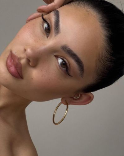 Maquillaje minimalista soft power con cejas marcadas, delineado sutil y labios nude mate.