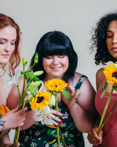 Tres mujeres sosteniendo flores y celebrando la amistad femenina en San Valentín, representando amor propio y Galentine’s Day.