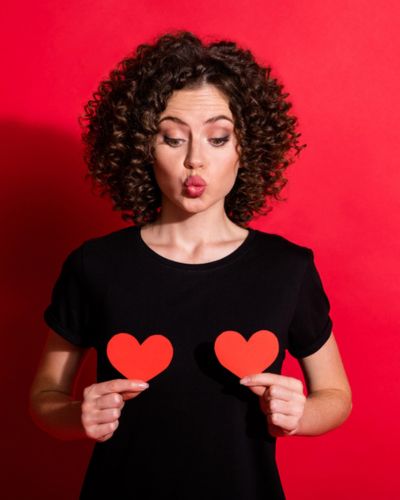Mujer soltera sosteniendo dos corazones rojos sobre fondo rojo en San Valentín, representando amor propio e independencia femenina.