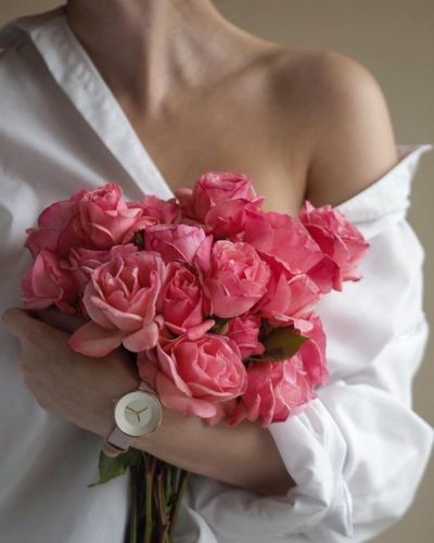 Mujer sosteniendo un ramo de rosas rosas frente al pecho, símbolo de feminidad y concientización sobre el cáncer de mama.