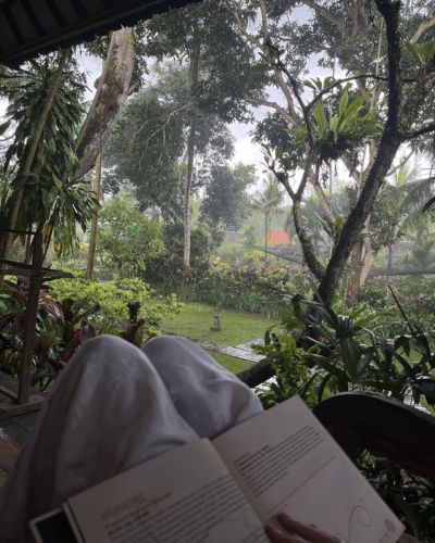 Persona leyendo un libro en una terraza rodeada de selva tropical durante vacaciones de descanso.