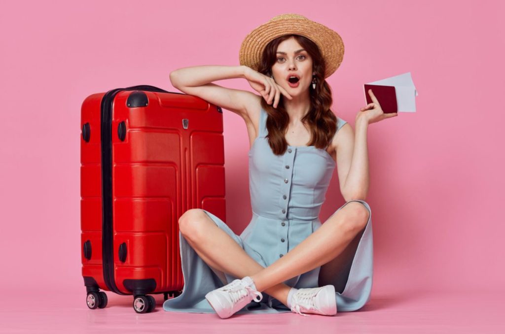 Mujer joven sentada en el piso con maleta roja y pasaporte en la mano, lista para viajar en Semana Santa.