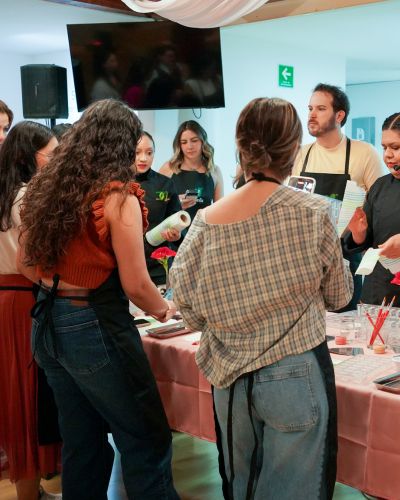 Grupo de personas en un taller de cocina observando a chefs con mandil mientras preparan postres en una mesa.