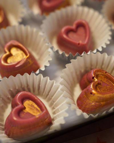 Chocolates en forma de corazón, en tonos rosa y dorado, acomodados en capacillos blancos.