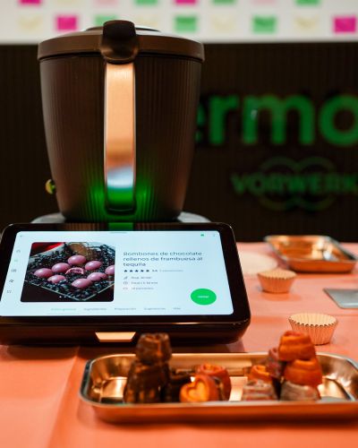 Thermomix sobre una mesa decorada, con pantalla mostrando una receta de bombones en la plataforma Cookidoo.