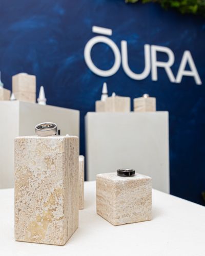 Anillo inteligente OURA Ring 4 sobre pedestal de piedra frente al logo de OURA, alternativa discreta al smartwatch.