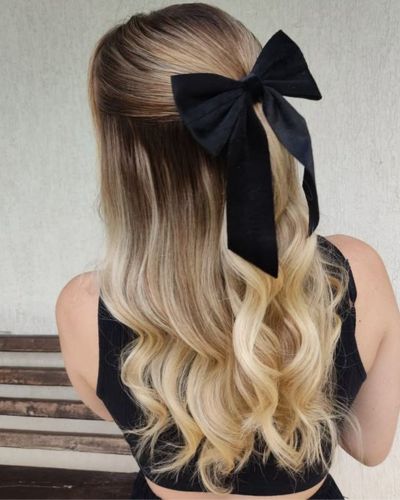 Cabello rubio con media cola y adornado con un listón negro 