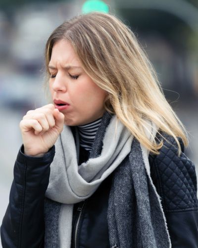 Mujer adulta con tos persistente, uno de los síntomas iniciales del sarampión.