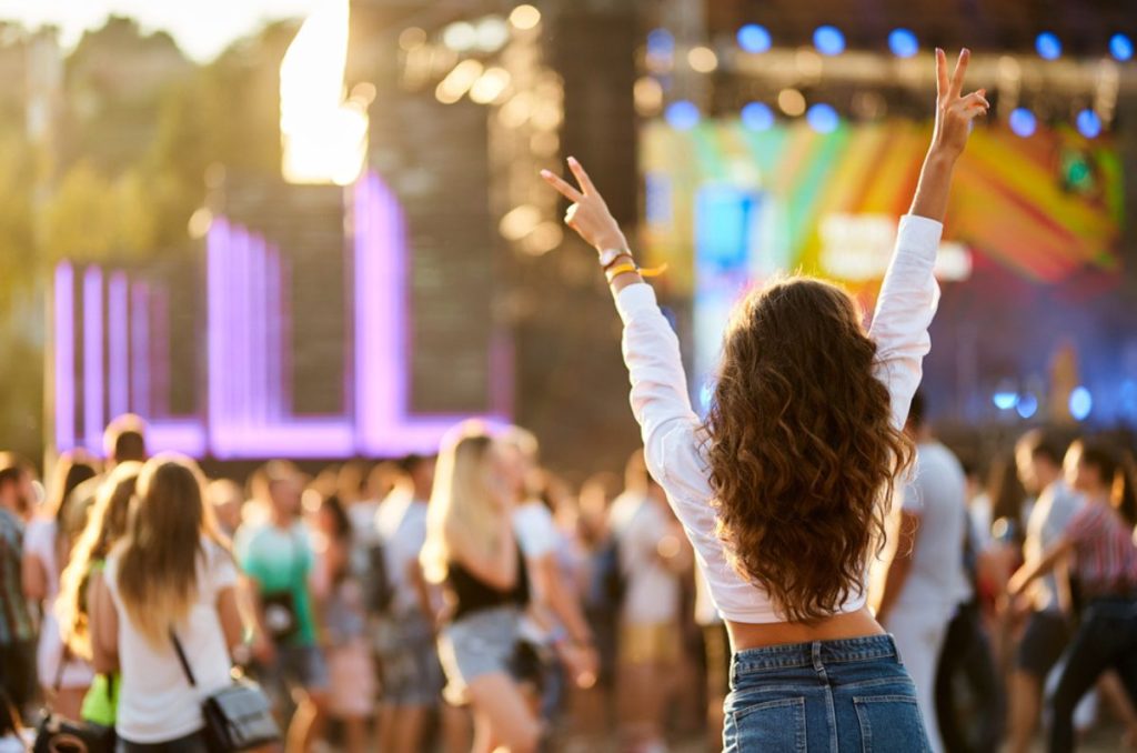 Mujer disfrutando un festival de música al aire libre en la CDMX con escenario iluminado y público celebrando en el Tecate Emblema 2026.