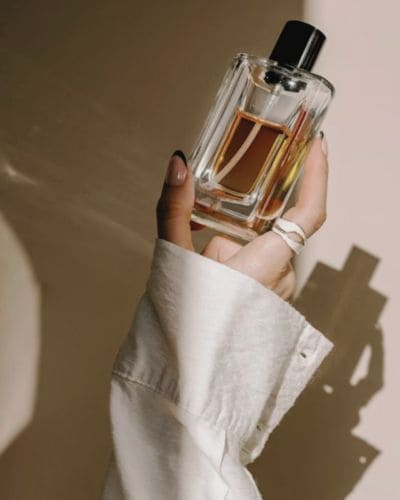 Mujer sosteniendo frasco de perfume y aplicándolo en atomizador, lista para el 14 de Febrero.