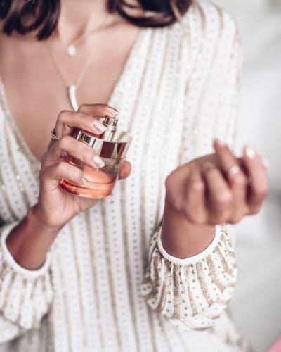 Mujer aplicando perfume en la muñeca antes de una salida romántica en San Valentín.