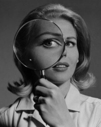 Mujer observando su rostro con una lupa, simbolizando la percepción y autoimagen corporal.