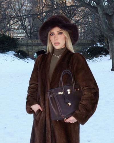 Modelo posando con bolsa Hermès Birkin café en escenario invernal.