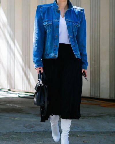 Saco azul intenso combinado con falda negra midi y botas blancas altas.