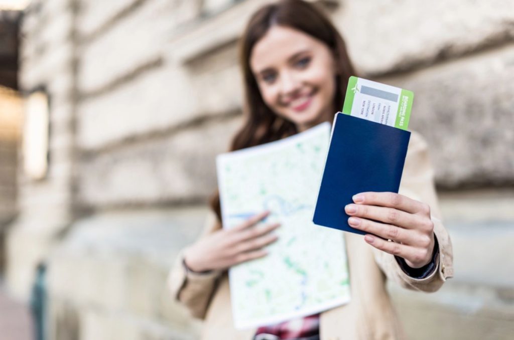 Mujer joven sosteniendo un pasaporte y un pase de abordar mientras lleva un mapa durante un viaje.