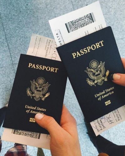 Dos manos sosteniendo pasaportes estadounidenses y boletos de avión en un aeropuerto.