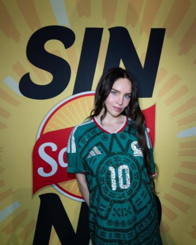 Belinda posando con jersey verde con el número 10 frente a un fondo amarillo con logo de marca.