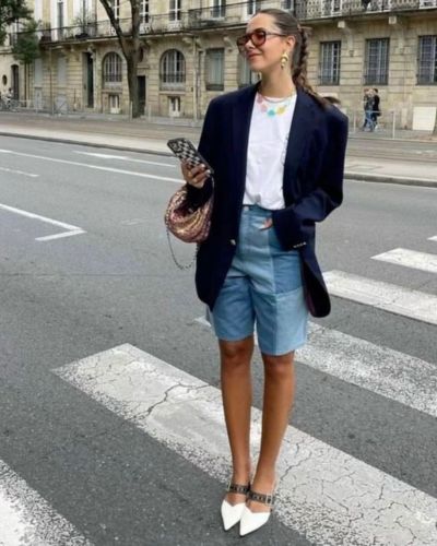 Modelo viste look de bermudas de mezclilla con blazer negro y t-shirt blanca básica.