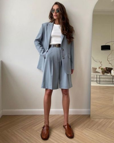 Modelo viste bermudas sastre de mujer en color gris, junto a un blazer oversize y una playera blanca lisa y accesorios neutros.