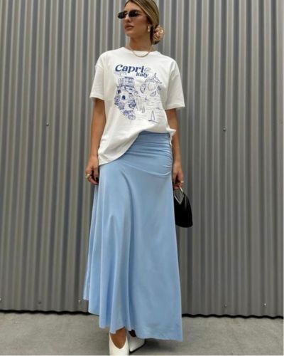 Modelo viste camiseta gráfica oversized en color blanco y una falda midi en color azul.