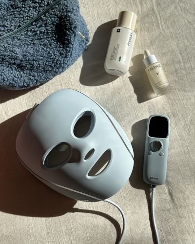 Dispositivo Shark CryoGlow sobre una superficie junto a su control y productos de skincare; composición minimalista.